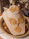 Golden tatted lace rose necklace displayed on a linen jewelry stand