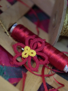 Tatted red and yellow poinsettia pin displayed with festive ribbon