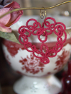 Lace heart ornament in deep red shown against romantic tabletop props.