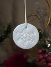 Pearlescent round ornament featuring a raised tatted lace snowflake design