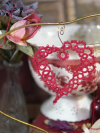 Handmade lace heart in red thread shown among vintage décor.