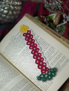 Hand-tatted Christmas candle lace bookmark resting on open vintage book.