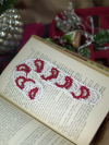 Delicate tatted lace candy cane bookmark placed on an open book for a festive wi