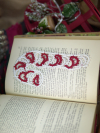 Red and white tatted candy cane bookmark lying on an open book with soft holiday