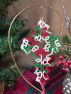Red, green, white tatted lace cross bookmark hanging in front of Christmas backg