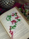 Delicate Christmas cross bookmark tatted in red, green, and white placed on an o