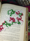 Intricately tatted Christmas cross bookmark set on an open book with holiday déc