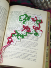Hand-tatted lace Christmas cross bookmark in red, white, and green resting on th