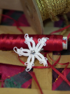 White tatted star pin with crystal center beside gold trim spool