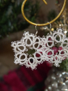 Detailed tatted snowflake earrings hanging from a gold earring holder.