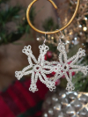 Hand-tatted silver snowflake earrings hanging on a gold display hook.