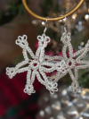 Sparkle-thread tatted snowflake earrings with winter décor background.