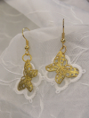 Brass and thread earrings with butterfly design on brown background.