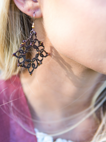 Close-up of handmade brown lace earrings in sunlight.