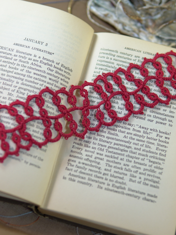 Handmade red tatted lace bookmark displayed across open vintage book pages