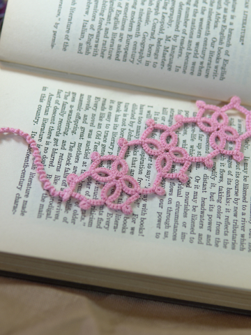 Pink tatted lace Josephine Knot bookmark resting on the pages of an open book