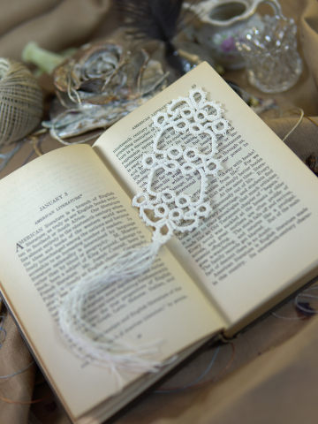 White tatted lace bookmark with tassel resting across pages of an open book