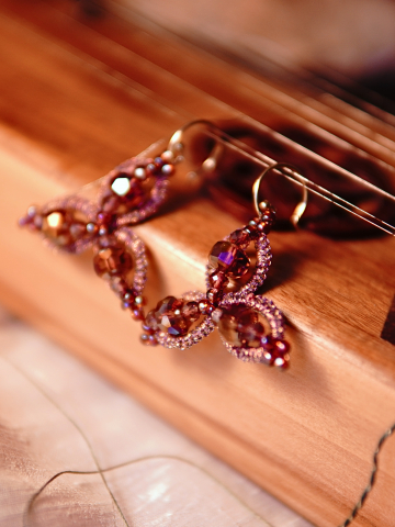 Pink tatted earrings with crystals resting on a wooden instrument.