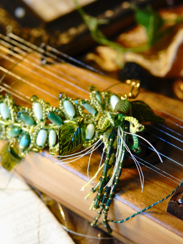 Green tatted leaf necklace with crystals displayed on stringed instrument