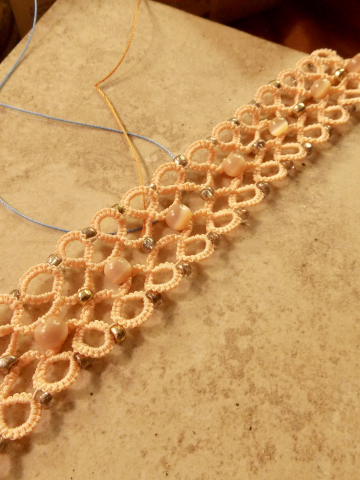 Tatted lace bracelet in coral thread with shining beads on stone tile