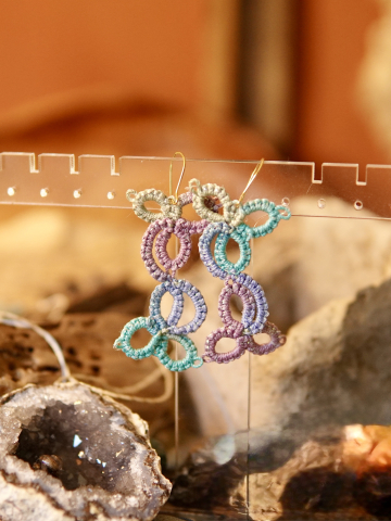 Pastel earrings displayed in front of a bohemian background.
