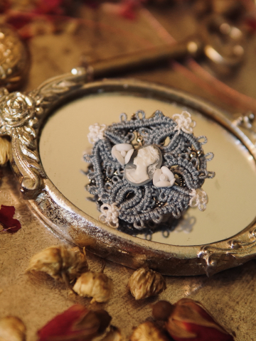Blue tatted lace cameo brooch on a silver mirror with clay flowers
