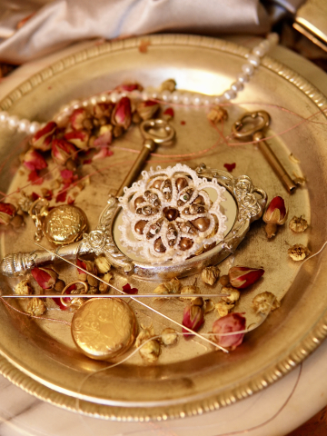Ornate lace brooch with cloisonné and pearls on a silver mirror tray