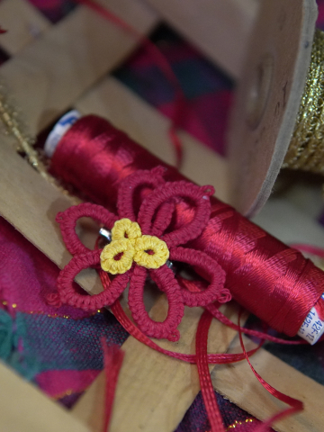 Tatted red and yellow poinsettia pin displayed with festive ribbon
