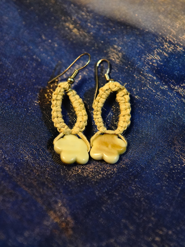 Tatted hemp earrings with star-shaped shell beads on blue fabric.